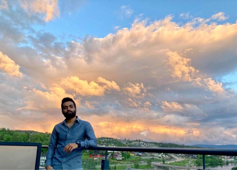 Arjun Ajith on a rooftop terrace under a dramatic sunset sky over a Norwegian town